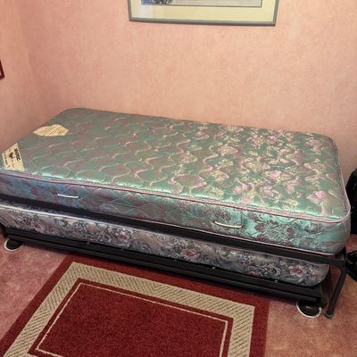 Vintage twin-size trundle bed with floral-patterned mattresses on a metal frame.