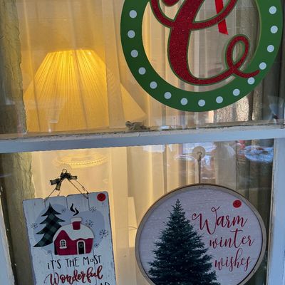 Assorted Christmas window decorations, including a green and red glitter monogram "C" wreath, a rustic wooden sign reading...