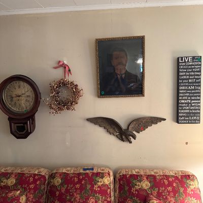 Assorted wall decor including a vintage regulator-style wall clock, a framed portrait of a man, a cast metal eagle wall hanging, and a...