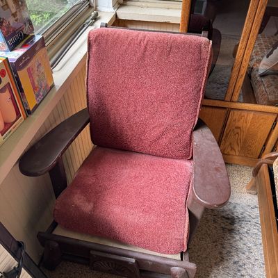 Vintage wooden chair with faded reddish-pink fabric cushions, showing wear on the armrests and frame.