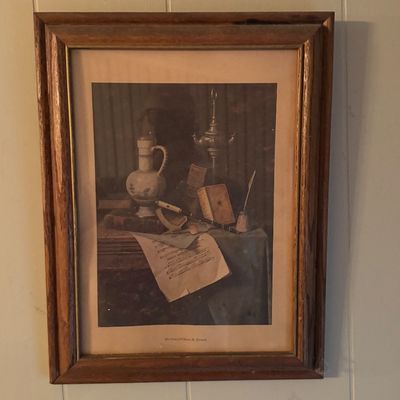 Framed still life print by William Michael Harnett, featuring a composition of books, a pitcher, sheet music, and a quill, housed in a...