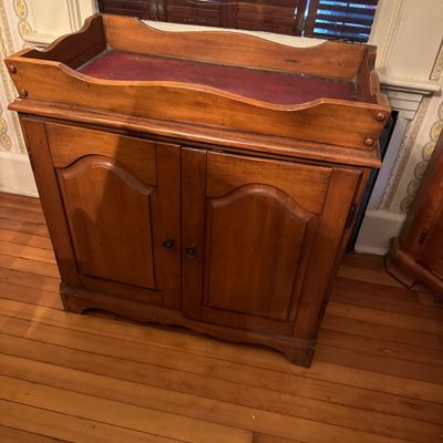 Vintage wooden dry sink cabinet featuring a two-door lower storage area and a recessed top lined with a reddish-brown surface.