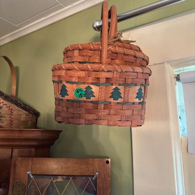 Vintage woven basket with a lid, featuring a decorative band of green evergreen trees and a sturdy carrying handle.