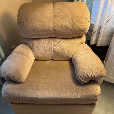 Overstuffed beige fabric recliner armchair, showing some wear and a small tear on the front seat cushion.