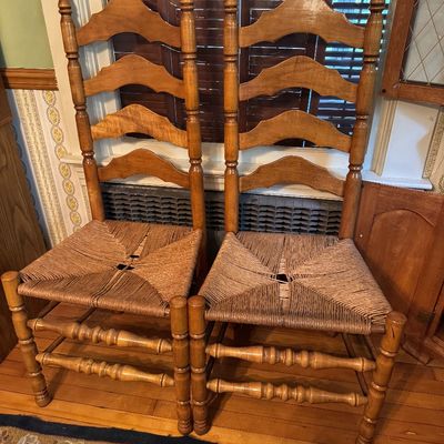 Pair of vintage colonial-style ladderback dining chairs featuring woven rush seats, turned legs, and finial-topped posts.