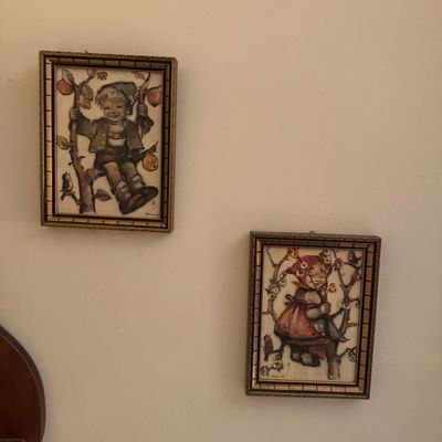 Pair of vintage framed Hummel-style prints featuring a boy and a girl sitting in apple trees, housed in ornate gold-toned frames.