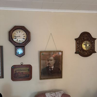 Assorted wall decor including an octagonal regulator-style wall clock, an ornate carved wood wall clock, an antique framed portrait of a...