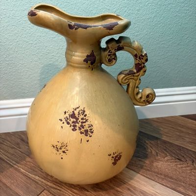 Sale Photo Thumbnail #49: Tuscan-style ceramic pitcher with a distressed yellow glaze, ornate scroll handle, and dark brown sponge-painted accents.