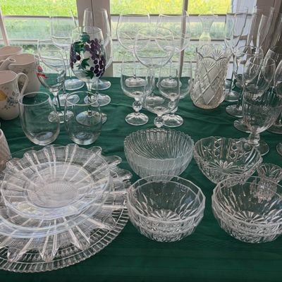 Sale Photo Thumbnail #60: Assorted vintage glassware collection, including cut glass bowls, plates, a crystal vase, and various wine and champagne glasses displayed on a green tablecloth.