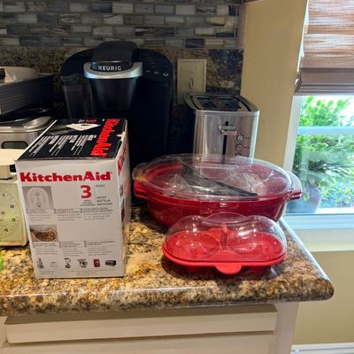 Sale Photo Thumbnail #28: Assorted kitchen appliances including a boxed KitchenAid 3-speed hand mixer, a Keurig coffee maker, a stainless steel toaster, and red microwave cookware.