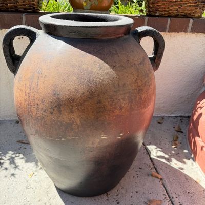 Sale Photo Thumbnail #22: Large rustic terracotta amphora jar with a distressed brown and black finish and two side handles, suitable for outdoor garden decor.