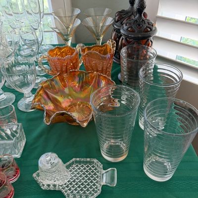 Sale Photo Thumbnail #59: Assorted vintage glassware collection, featuring marigold carnival glass pieces, clear ribbed tumblers, stemmed wine glasses, and decorative pressed glass items.