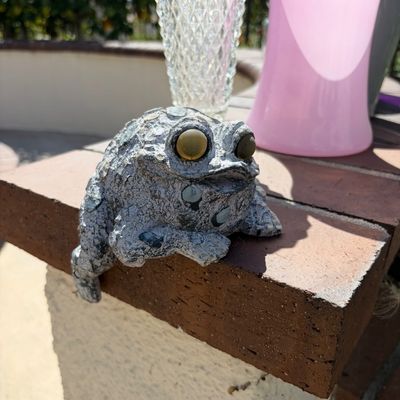 Sale Photo Thumbnail #20: Whimsical concrete frog garden statue with large glass eyes, designed to sit on the edge of a brick wall or planter.