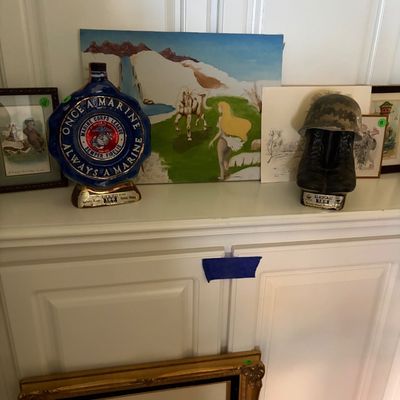 Sale Photo Thumbnail #74: Collection of military memorabilia and artwork, featuring a Jim Beam "Once a Marine, Always a Marine" decanter and a combat boot and helmet decanter, displayed alongside framed prints and paintings.