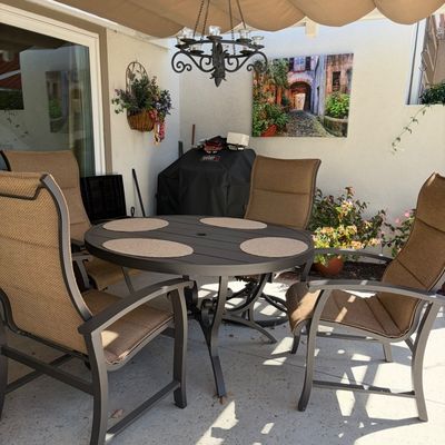 Sale Photo Thumbnail #16: Outdoor dining set featuring a round dark metal table with four matching high-back swivel chairs upholstered in tan mesh fabric.