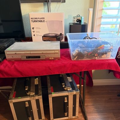 Sale Photo Thumbnail #86: Sony DVD/VCR combo player, a boxed record player turntable, a plastic bin of assorted cables, and two heavy-duty road cases.
