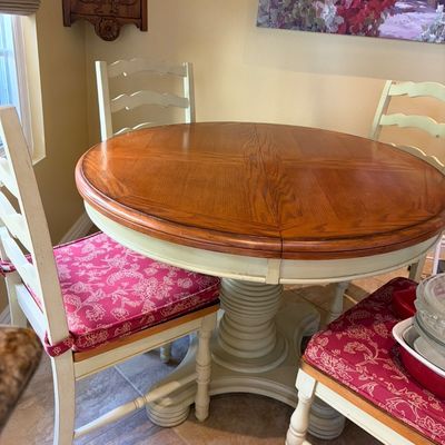 Sale Photo Thumbnail #27: Country-style round pedestal dining table with a natural wood top and off-white base, paired with matching ladder-back chairs featuring red floral cushions.