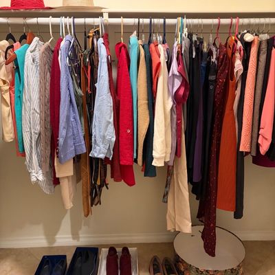 Sale Photo Thumbnail #72: Assorted women's clothing hanging on a closet rack, featuring colorful blouses, sweaters, and dresses, with shoes in boxes and a floral hatbox below.