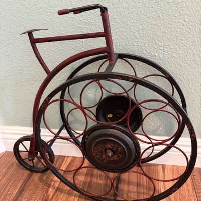 Sale Photo Thumbnail #64: Vintage-style metal wine rack shaped like a penny-farthing bicycle, featuring a distressed red and black finish with slots for up to six bottles.