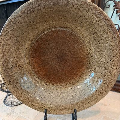 Sale Photo Thumbnail #44: Large studio art pottery charger with a textured, speckled beige rim and a contrasting rust-brown center, displayed on a black metal stand.