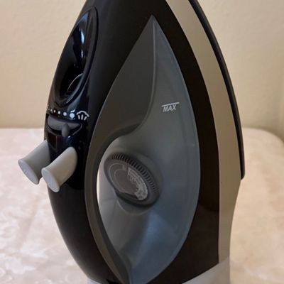 Sale Photo Thumbnail #68: Modern steam iron in black and grey with a retractable cord, shown standing upright on a table.