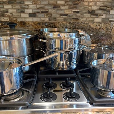 Sale Photo Thumbnail #33: Multi-piece set of stainless steel cookware, including stockpots, saucepans, and a steamer insert, displayed on a KitchenAid gas cooktop.