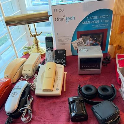 Sale Photo Thumbnail #85: Assorted vintage and modern electronics, including a brass desk lamp, several corded and cordless landline telephones, a Sony Dream Machine clock radio, over-ear headphones, and a boxed Omnitech digital photo frame.