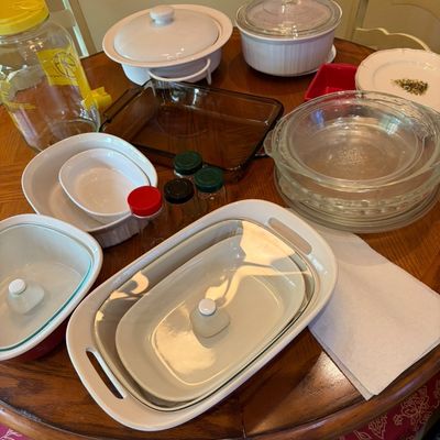 Sale Photo Thumbnail #34: Assorted kitchen bakeware and glassware, including CorningWare casserole dishes, Pyrex pie plates, and a glass beverage dispenser, displayed on a wooden table.