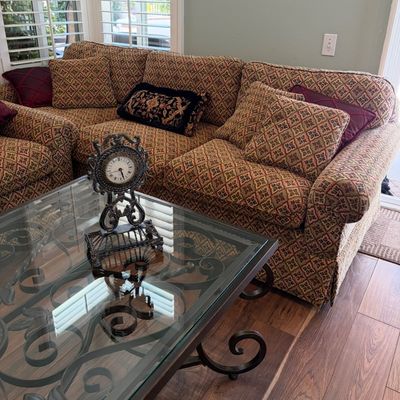 Sale Photo Thumbnail #57: Traditional patterned sectional sofa with matching throw pillows, paired with a wrought iron and glass-top coffee table featuring a decorative metal table clock.