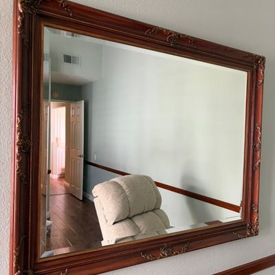 Sale Photo Thumbnail #39: Large rectangular wall mirror featuring an ornate reddish-brown wooden frame with gilded, decorative corner and edge accents.