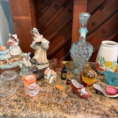 Sale Photo Thumbnail #65: Assortment of vintage collectibles and glassware, including porcelain figurines, a grape-shaped glass decanter, a floral vase, and various small decorative knick-knacks.