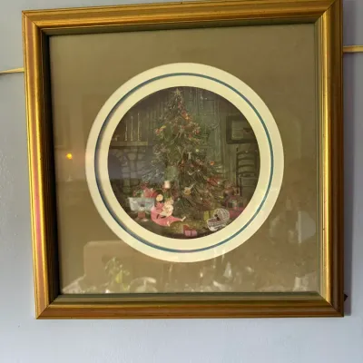 Framed circular Christmas print featuring a decorated tree and children opening gifts, housed in a square gold-finished frame with a...