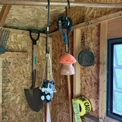 Assorted garden decor and tools hanging in a shed, including a ceramic mushroom, a hanging cat figurine, a shovel, and a roll of caution...
