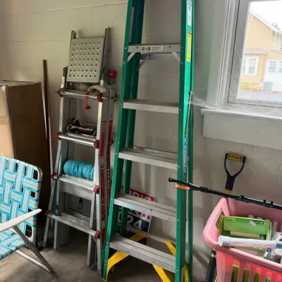 Werner 6-foot green fiberglass stepladder alongside a Little Giant multi-position aluminum ladder in a garage setting.