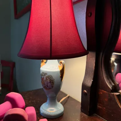 Vintage porcelain urn-style table lamp featuring a light blue base with a romantic scene illustration, gold-tone handles, and a deep red...