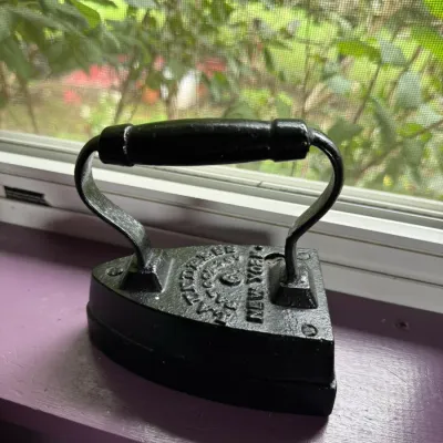 Antique cast iron sad iron with a black painted finish and wooden handle grip, featuring embossed lettering on the top plate.