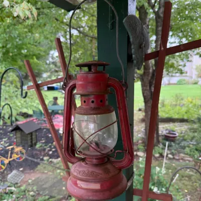 Vintage red metal kerosene lantern with a clear glass globe, showing some rust and wear from outdoor use.