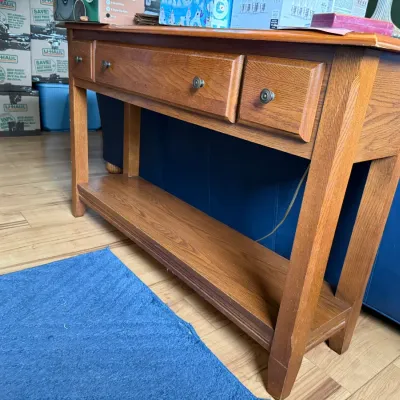 Mission-style oak console table featuring three drawers with round metal pulls and a lower display shelf.