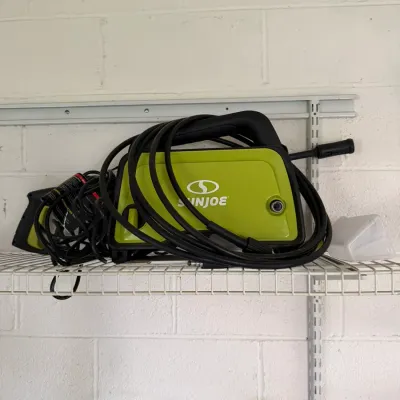 Sun Joe electric pressure washer in lime green and black, complete with hose and spray gun, stored on a wire shelf.