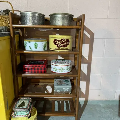 Vintage wooden folding baker's rack holding an assortment of collectible holiday and advertising tins, including Charles Chips and...
