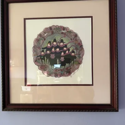 Framed and matted whimsical art print depicting a group of carolers in a circular, decorative border, housed in a dark wood frame.