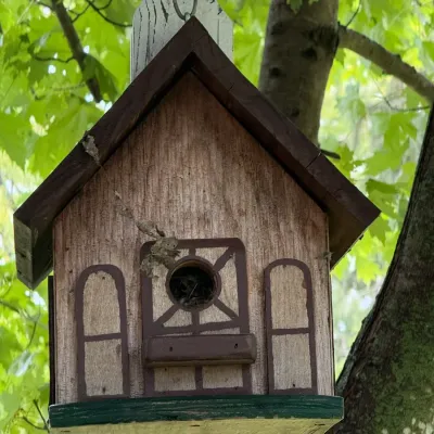 Rustic wooden birdhouse designed to look like a small cottage or barn, featuring painted trim details and a hanging chain.