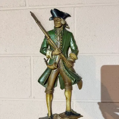 Vintage Sexton cast metal wall plaque depicting a Revolutionary War soldier in a green coat holding a musket, circa 1970s.