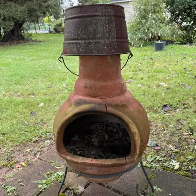 Rustic terracotta chiminea on a black metal stand, featuring a weathered metal bucket used as a rain cap.