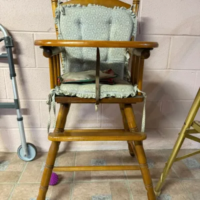 Vintage wooden high chair with a light green floral patterned cushion and a flip-over tray.