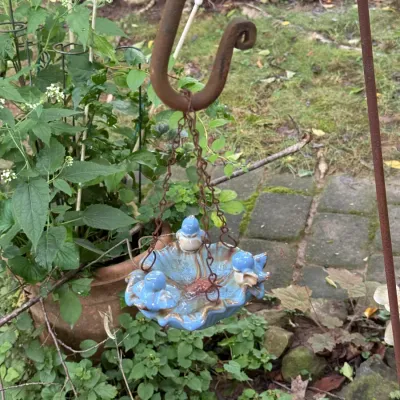 Small blue glazed ceramic bird feeder with three sculpted birds, hanging from a rusted metal chain and shepherd's hook.