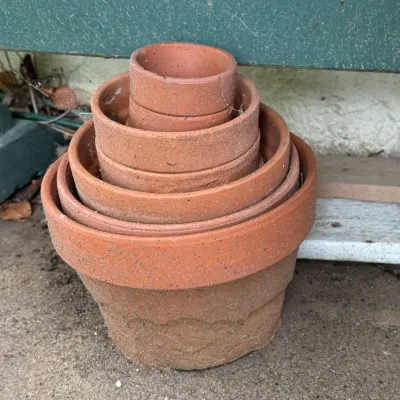 Stack of nested terracotta flower pots in various sizes, showing natural weathering and wear.