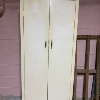 Vintage mid-century metal utility wardrobe cabinet in off-white paint with chrome handles and a black base.