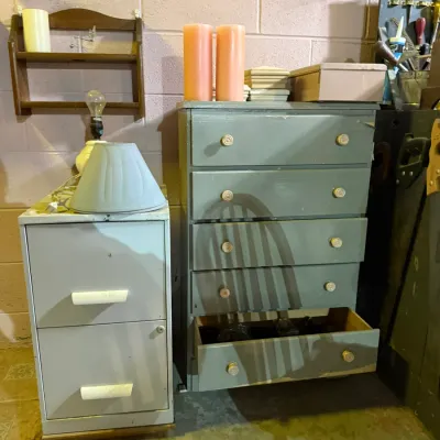 A light gray two-drawer metal filing cabinet alongside a five-drawer wooden dresser painted in a muted green-gray finish.