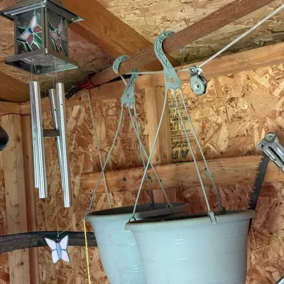 Two grey plastic hanging planter pots suspended from a wooden beam, alongside a metal wind chime with a stained glass top panel.